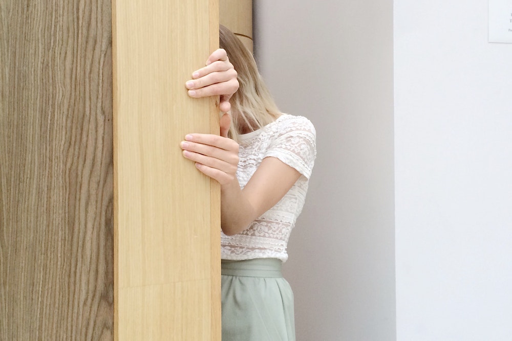 A Woman Hiding Behind A Wooden Furniture